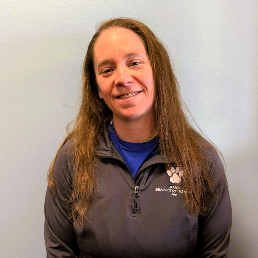 smiling woman with long brown hair standing in front of gray wall